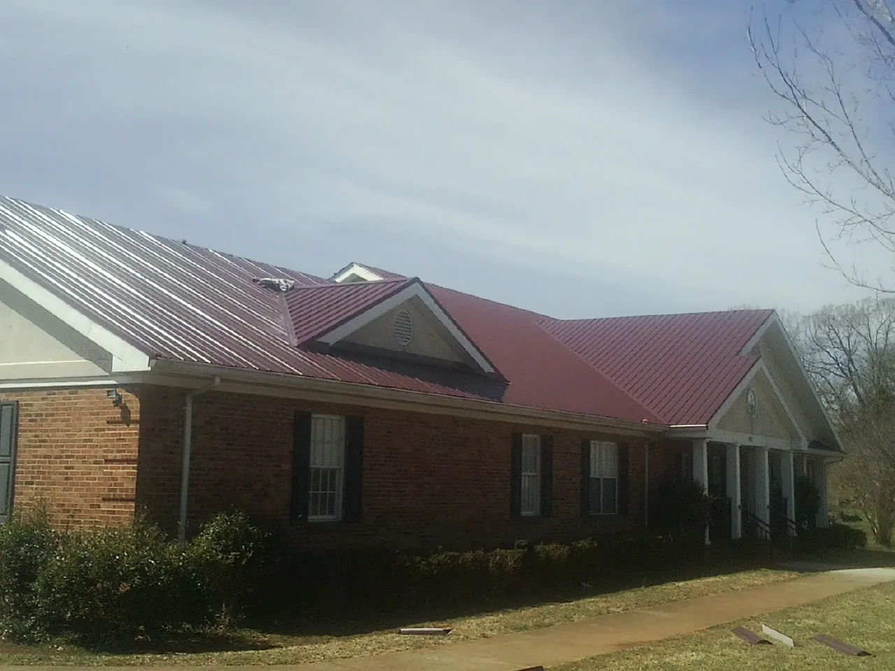 Red metal roof with gabled entries on a long brick building, from a Hail Damage Roof Repair job in Goldendale