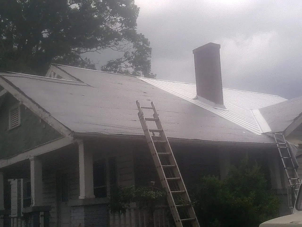 Ladders against a metal roof on an older home with a brick chimney in Goldendale
