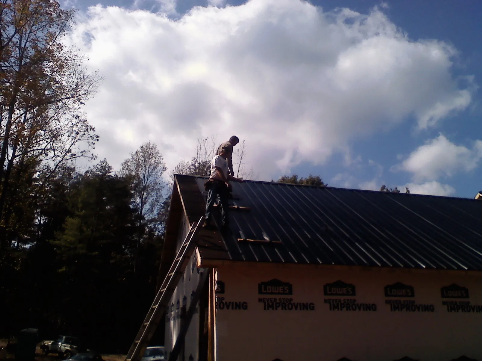 Roofer fastening dark metal panels high against a cloudy sky, from a Roof Inspection job in Goldendale