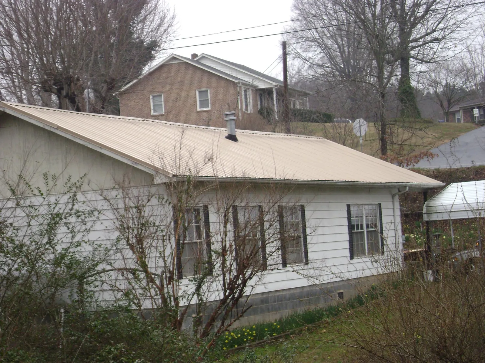 Tan metal roof on a white sided house set into a hillside — Commercial Roofing by Roofing Brothers in Goldendale